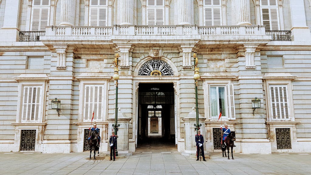 Donde Alojarse en Madrid en 2026 1 Guards and cavalry stand at the Royal Palace of Madrid entrance, showcasing Spanish heritage.