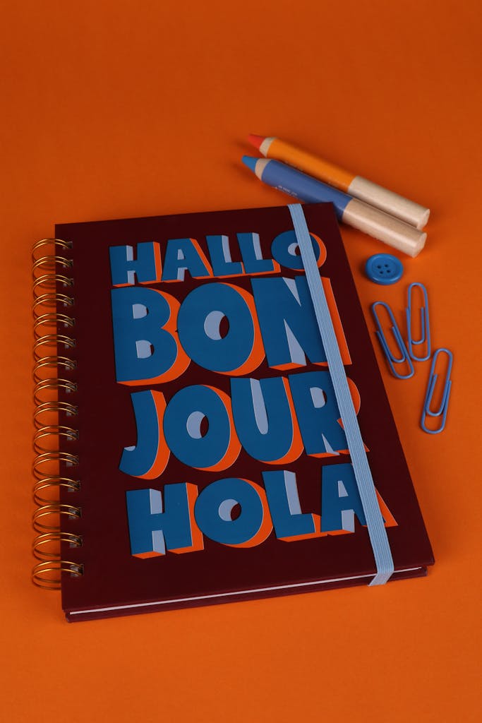 Resources 6 A vibrant notebook with greetings in multiple languages on an orange background, featuring stationery items.